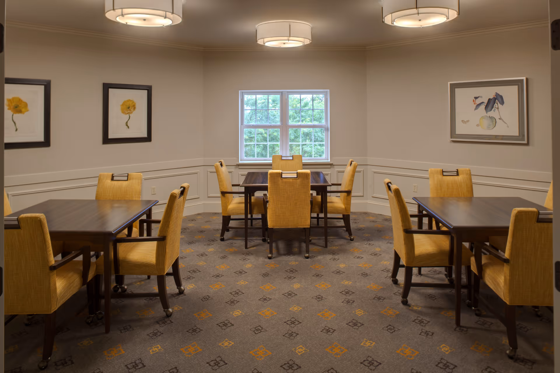 Small dining room with several wooden tables and yellow upholstered chairs arranged around a central window.