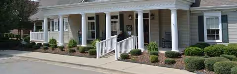 Front view of a single-story senior living facility with a covered porch and shrubs.