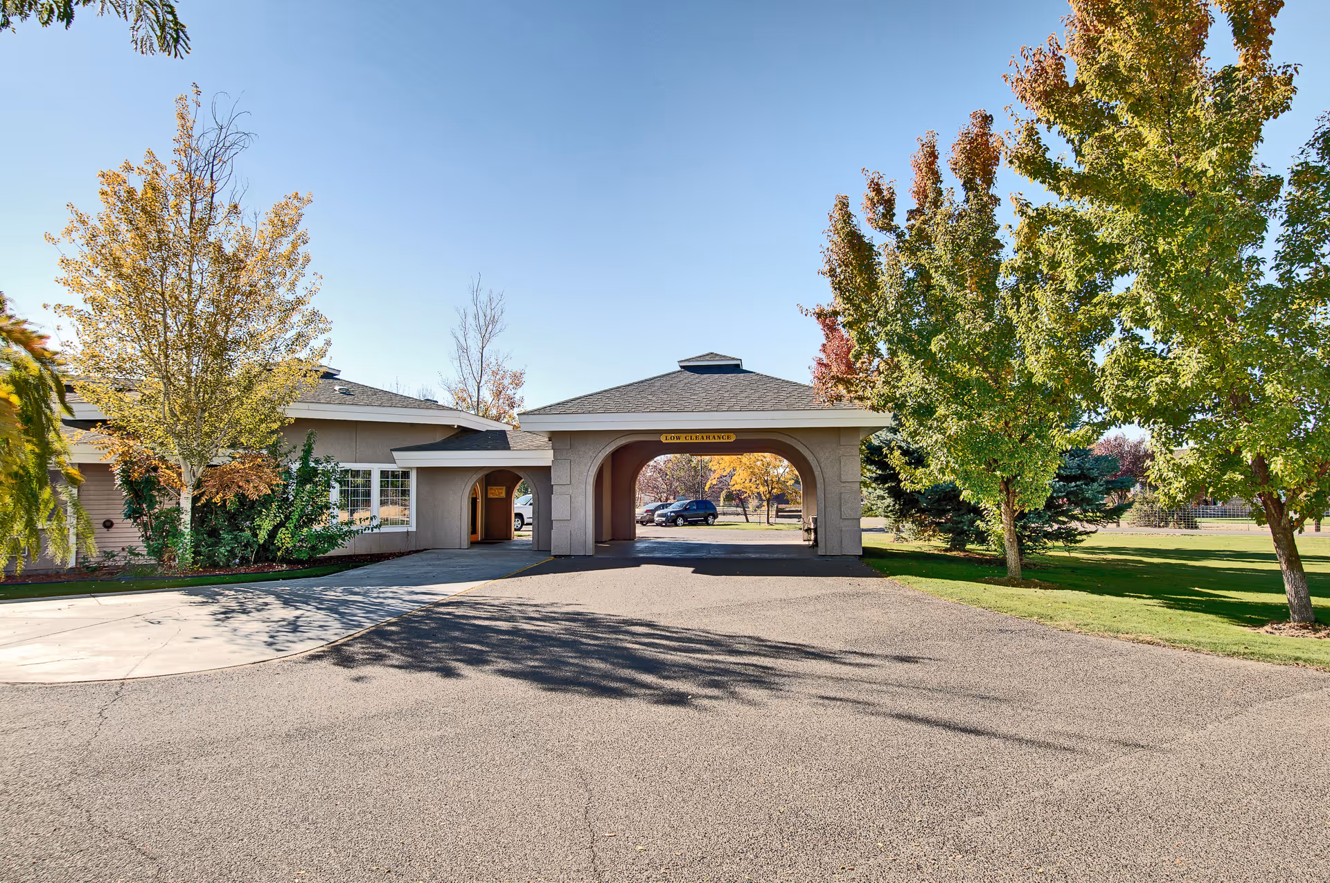 Exterior view of Wellsprings Assisted Living facility entrance with a covered driveway and surrounding trees with autumn foliage under a clear blue sky.