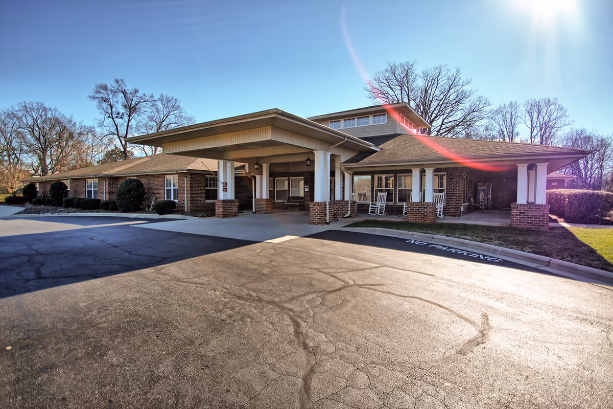Front entrance of a single-story brick senior living facility with a covered porte-cochère and rocking chairs on the porch.