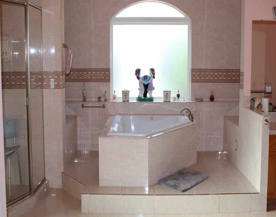 Tiled bathroom featuring a raised corner bathtub beneath a frosted arched window, a glass shower enclosure to the left, and decorative items on the tub ledge.