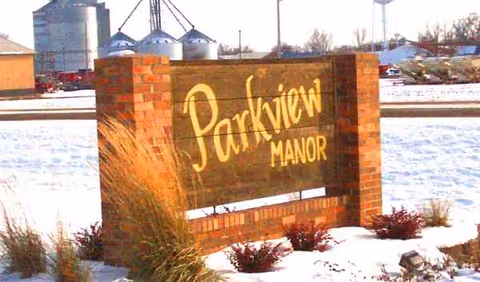 Parkview Manor brick entrance sign sits in a snowy landscape with surrounding shrubs