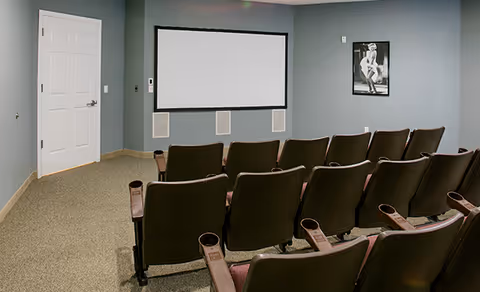 Small screening room with rows of theater seats facing a blank projection screen on a gray wall.