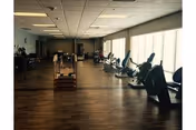 Spacious interior fitness room with cardio machines and strength equipment arranged on a wood floor beside large windows.