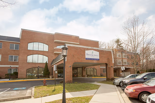 Front entrance of the Brookdale Potomac brick senior living building with a covered porte-cochère and parked cars.