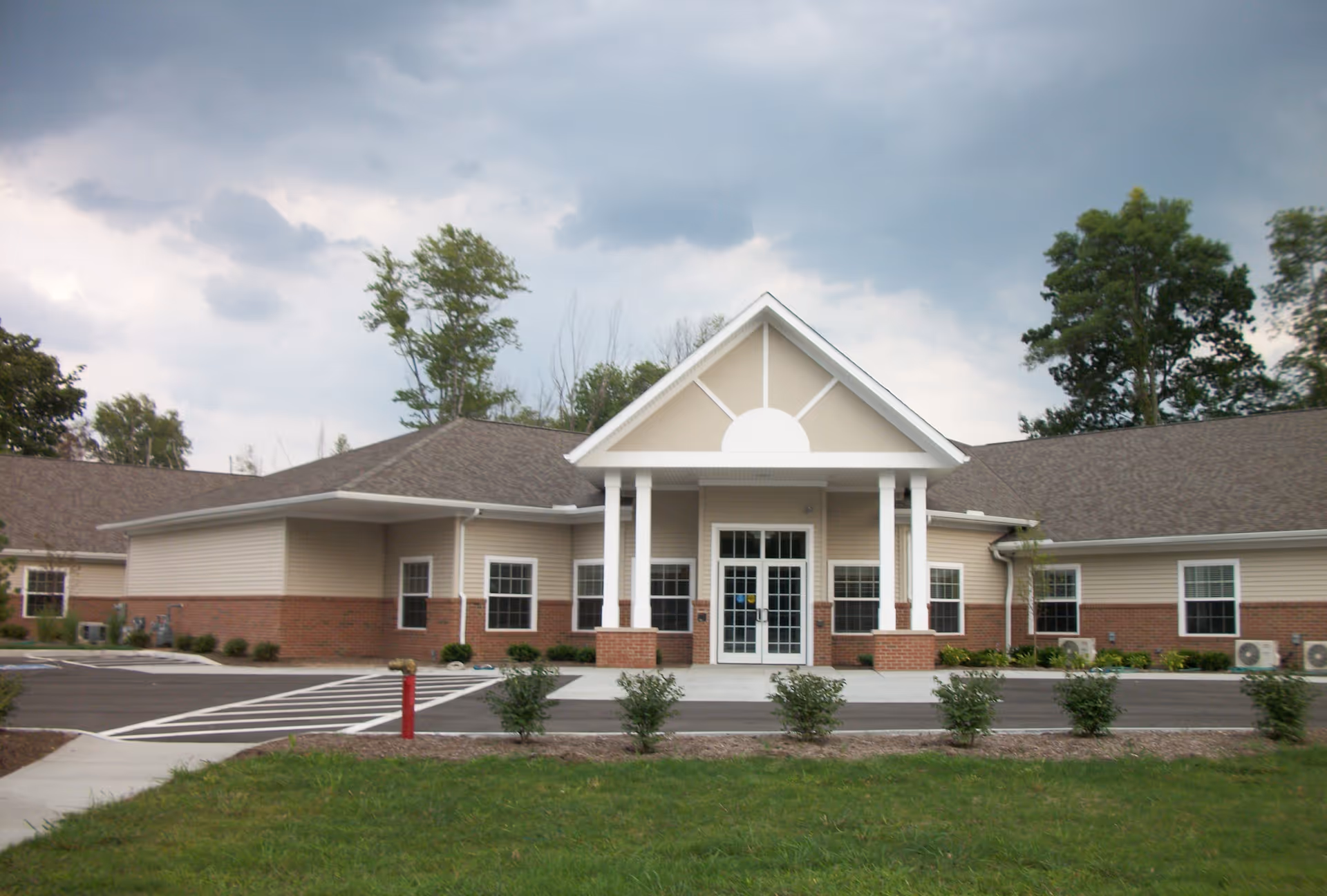 Front view of a single-story senior living facility with a covered entrance and parking.