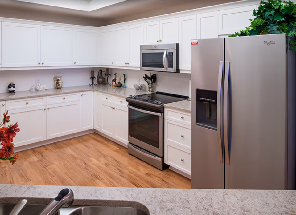 Bright modern kitchen with white cabinets, stainless steel refrigerator and stove, and a sink in the foreground.