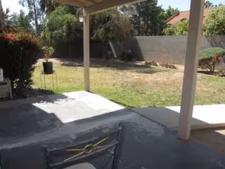 Shaded patio with concrete floor overlooks a grassy yard and privacy wall.