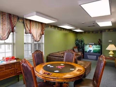 Common room with a round card table and four chairs, leather sofas, a television, and windows with patterned curtains.