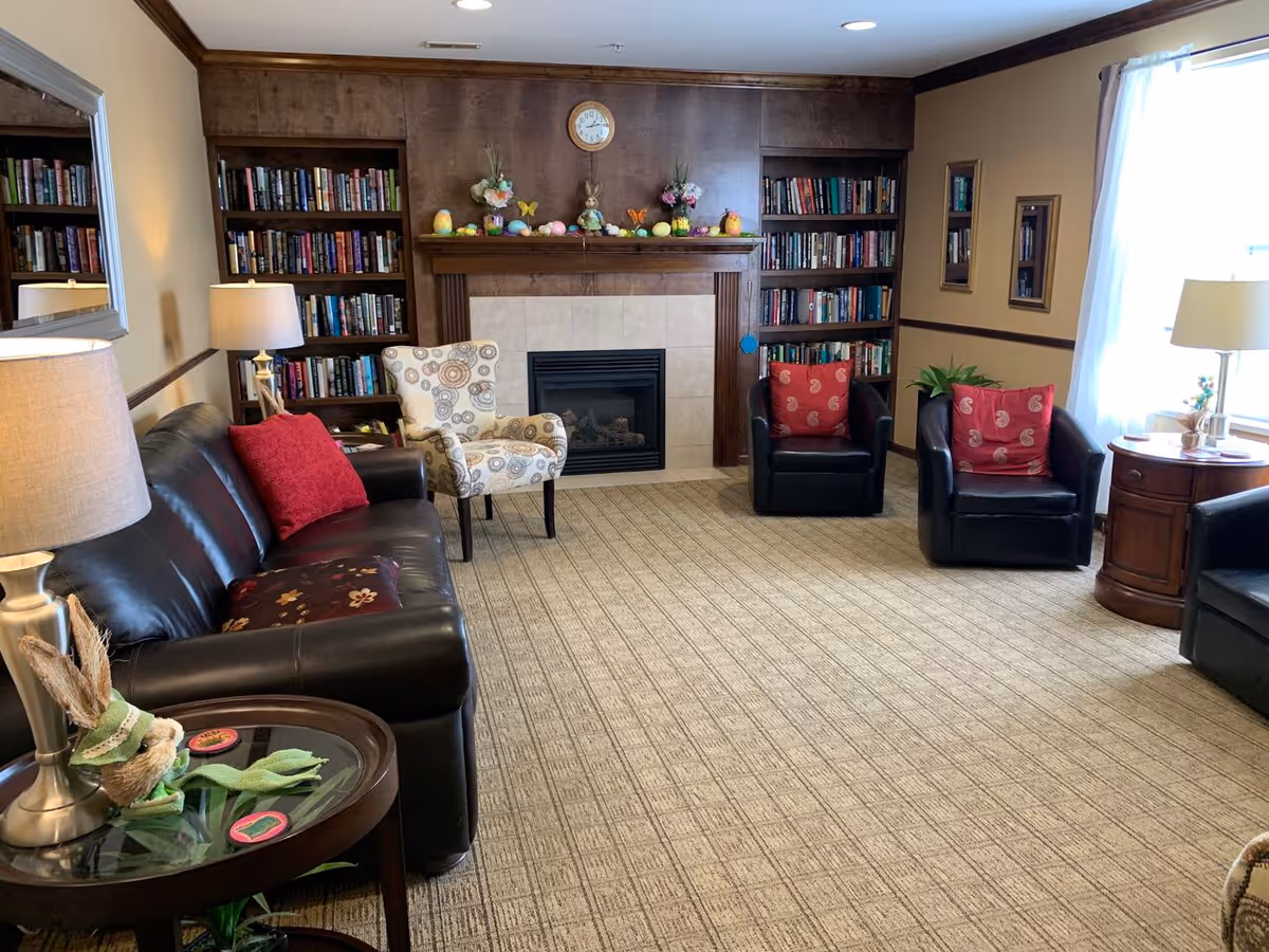 A cozy living room with leather sofas and armchairs arranged around a fireplace flanked by built-in bookshelves.