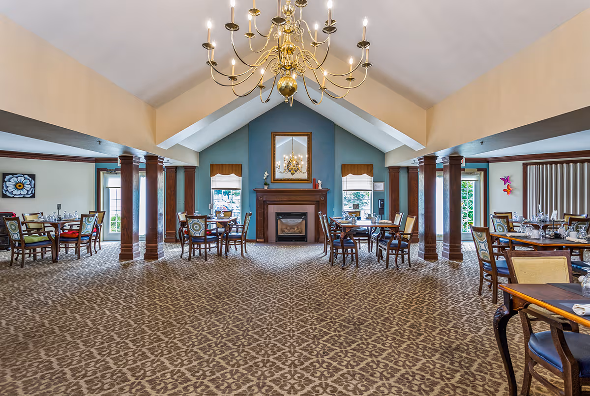 Spacious dining room with a vaulted ceiling and chandelier, a central fireplace, and multiple set tables and chairs.
