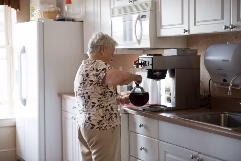 A person pouring coffee from a commercial coffee maker into a carafe at a kitchen counter.
