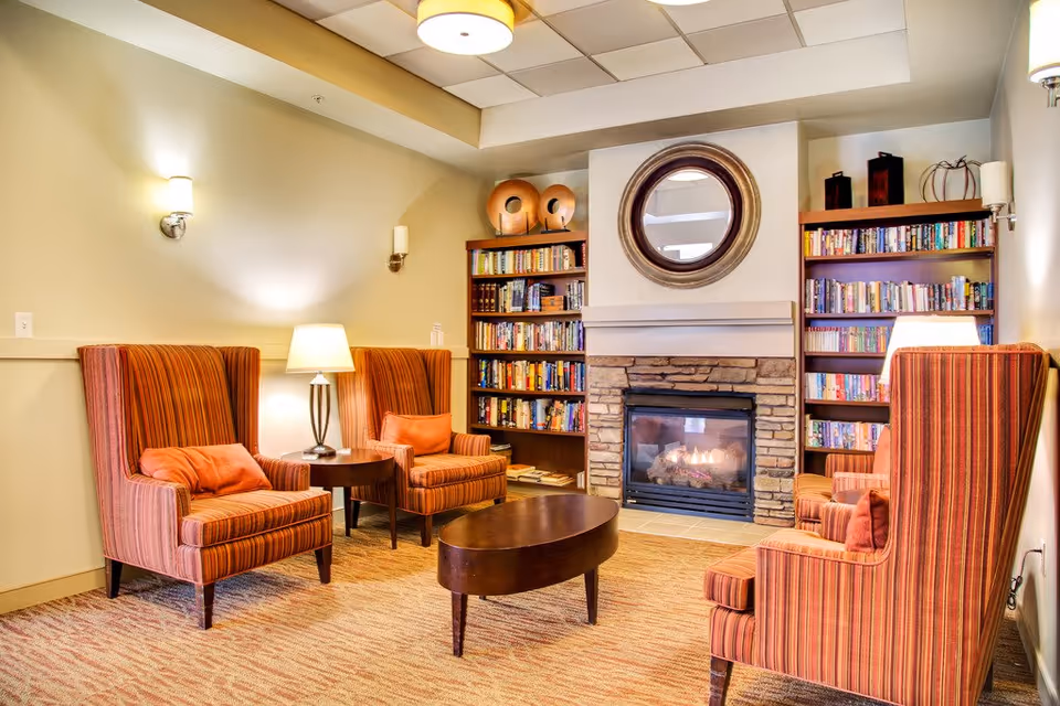 Cozy lounge with four striped armchairs arranged around a coffee table, bookshelves and a lit stone fireplace.