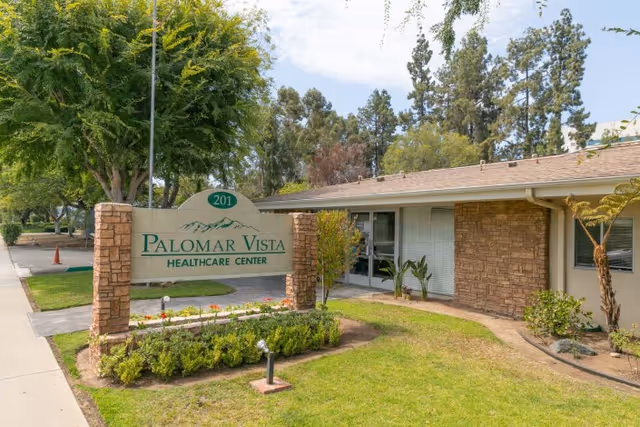 Sign and front entrance of Palomar Vista Healthcare Center surrounded by lawn, shrubs, and trees.