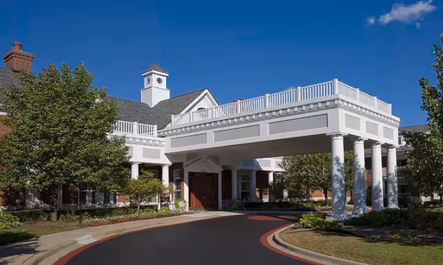 Front entrance of Waltonwood Twelve Oaks featuring a white-columned porte-cochere and building facade under a blue sky.