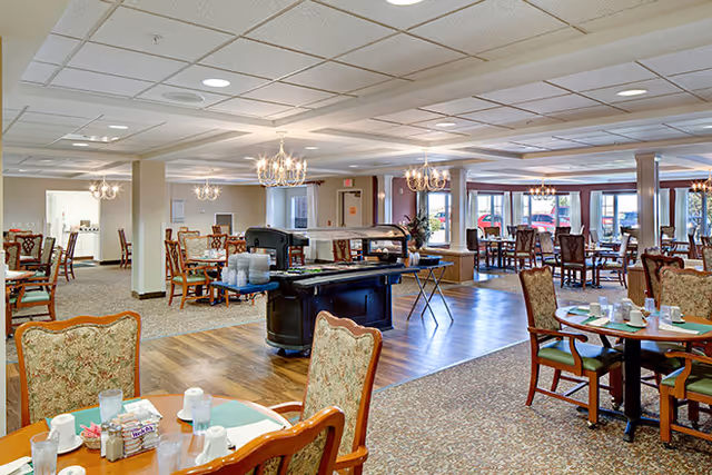Spacious dining room with multiple set tables and chairs, chandeliers, and a central serving cart.