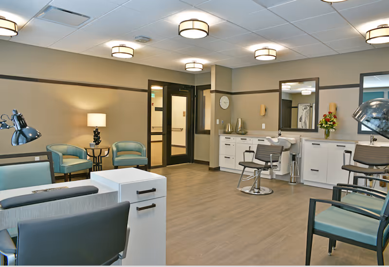 Well-lit salon area in a senior living facility with styling chairs, mirrors, cabinetry, and seating.