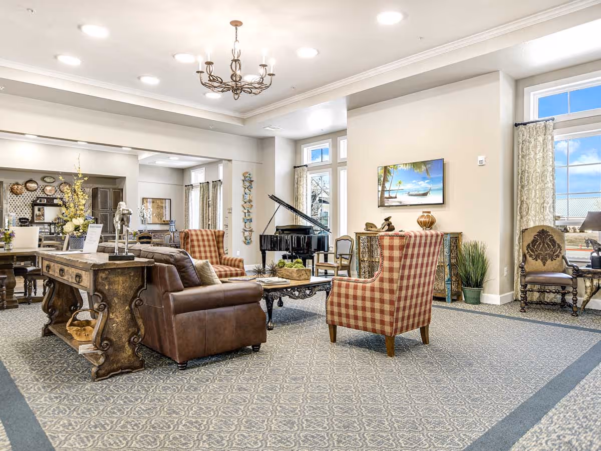 Bright, spacious common lounge with sofas, upholstered chairs, a grand piano and decorative furnishings.