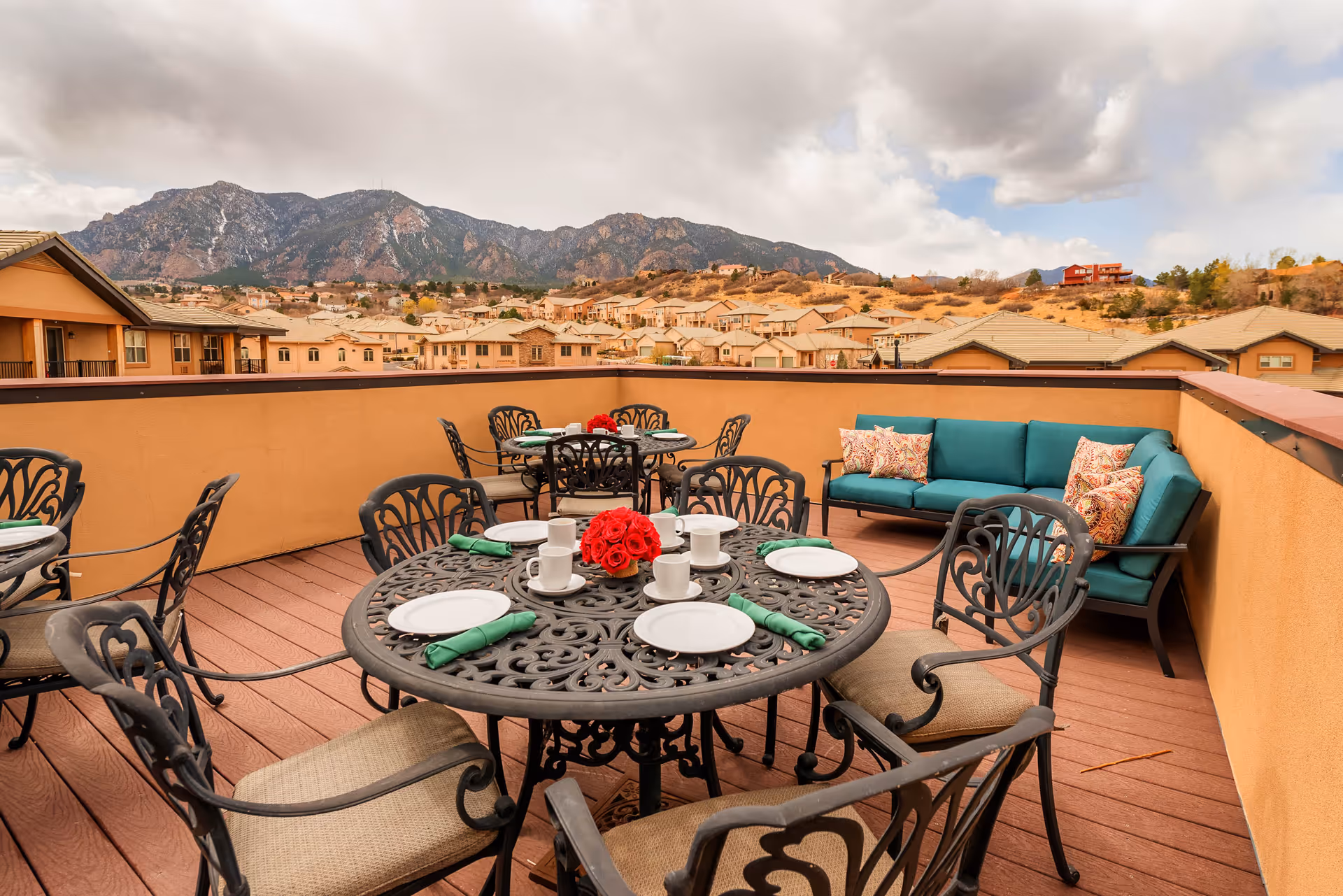 Rooftop patio with wrought-iron dining tables, place settings, and a teal cushioned sofa overlooking houses and mountains.