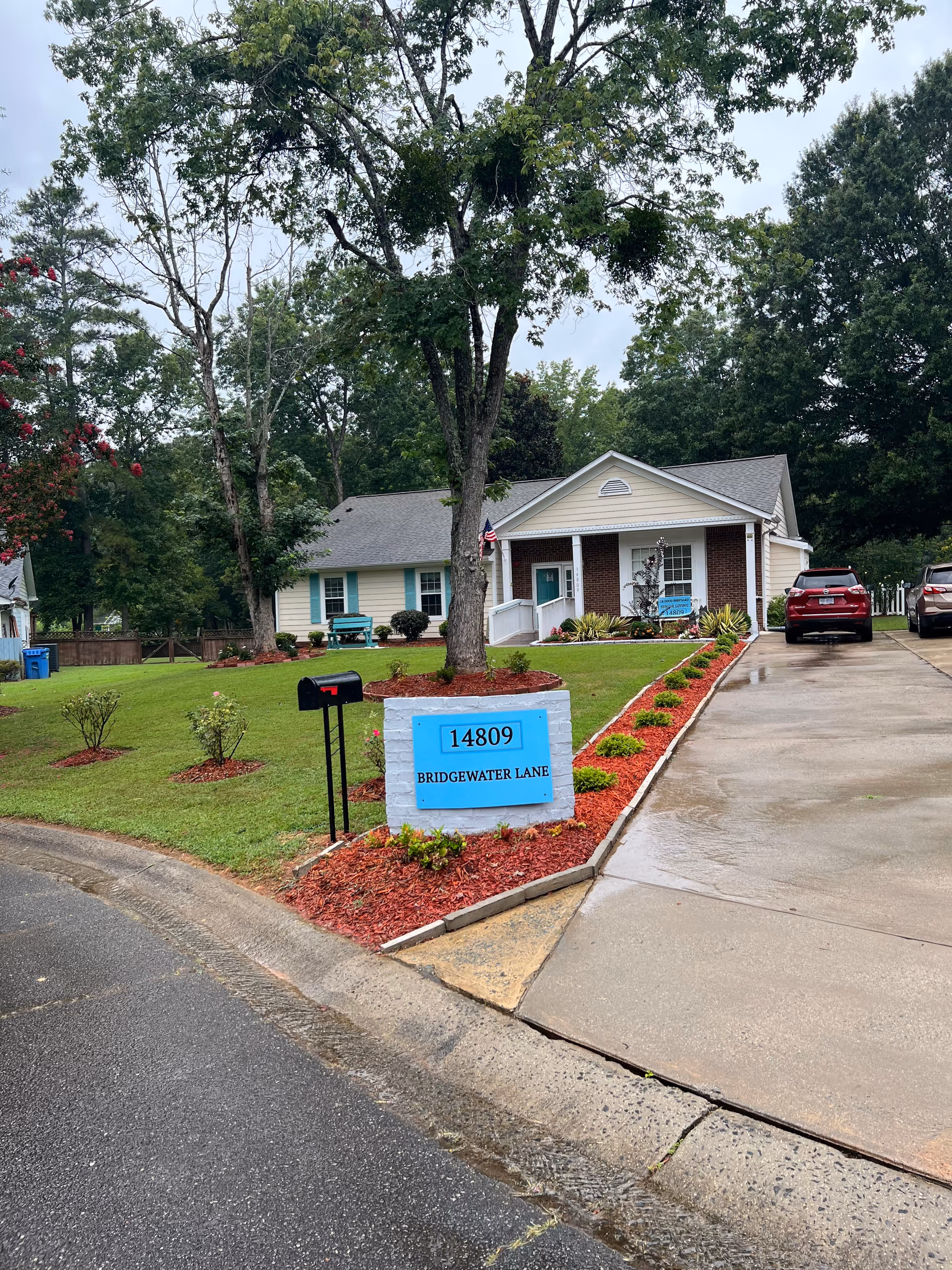 Front exterior of a single-story house with a driveway, mailbox, landscaped lawn and a blue sign reading "14809 Bridgewater Lane".
