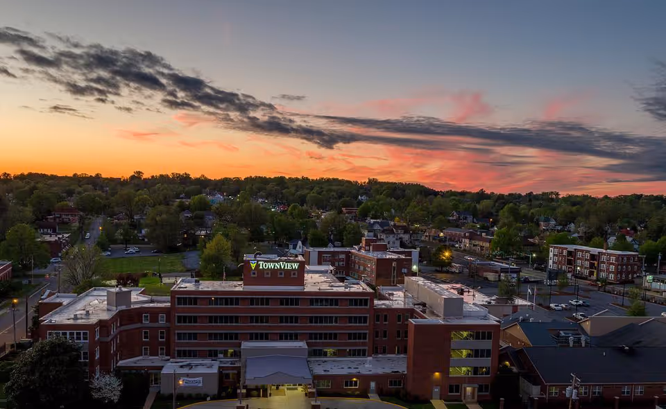 Aerial dusk view of the TownView Senior Living building and surrounding neighborhood under a colorful sunset sky.