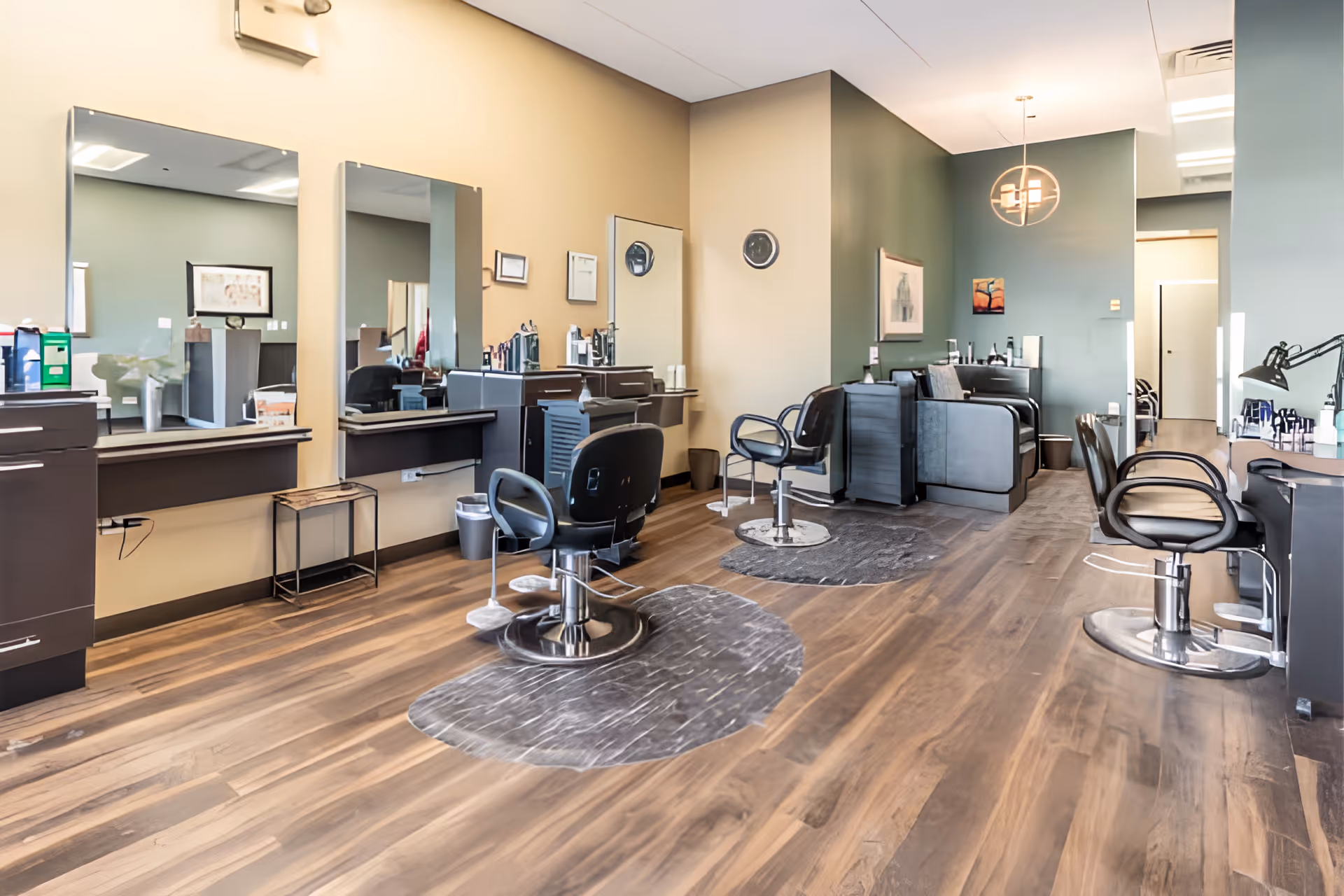 Well-lit salon area with multiple styling chairs, mirrors, and workstations on wood flooring.