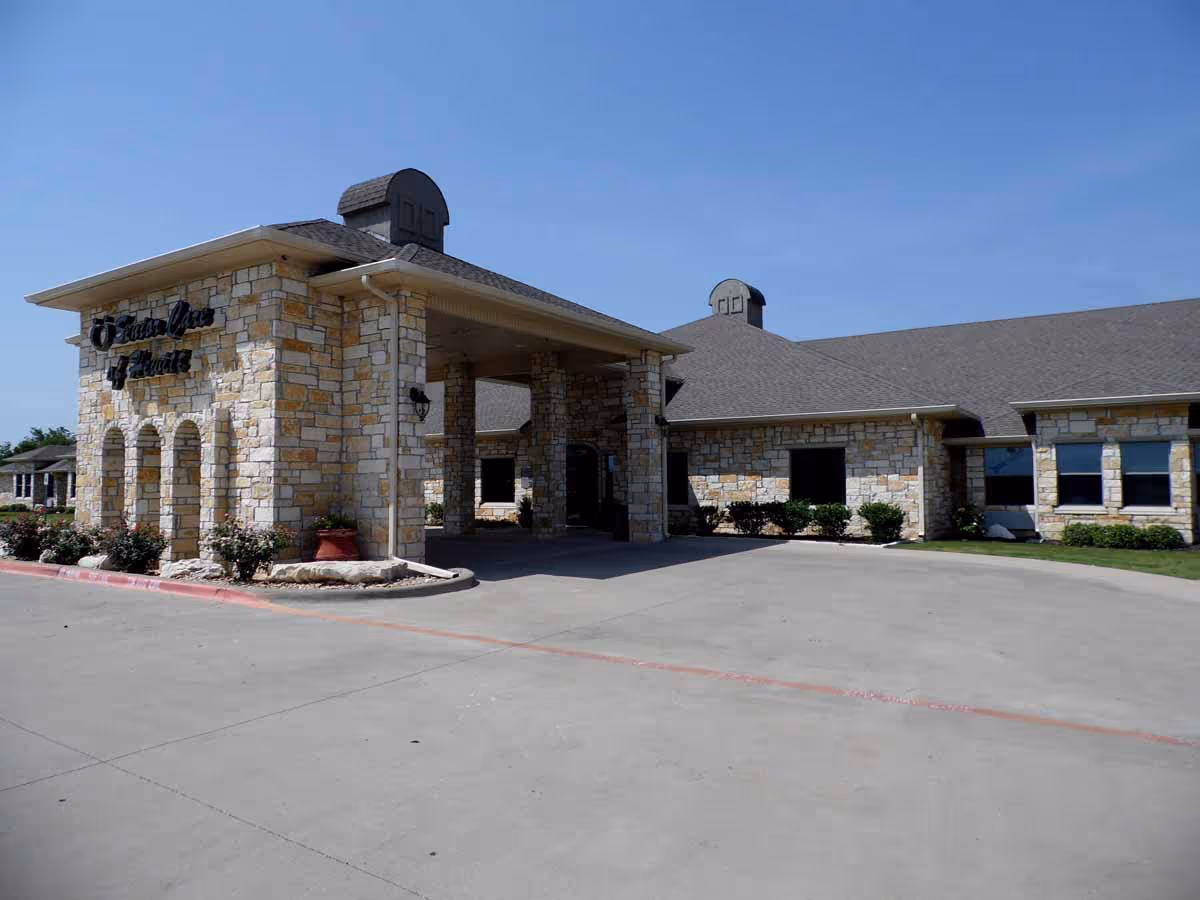 Exterior view of a stone building with a covered entrance and a driveway in front under a clear blue sky.
