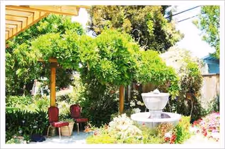 Outdoor garden area with a fountain, pergola, and red cushioned chairs.