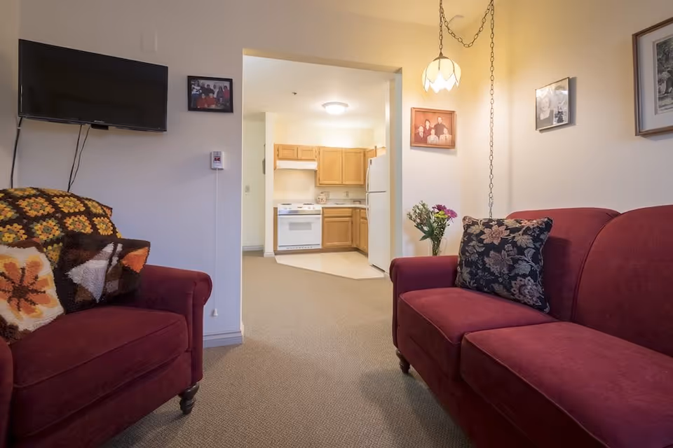 Cozy living room with two red upholstered sofas and a view through a doorway into a small kitchen.