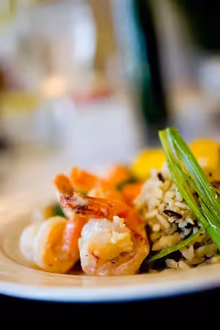 Close-up of a plate with cooked shrimp, wild rice, and green beans, with a blurred background.