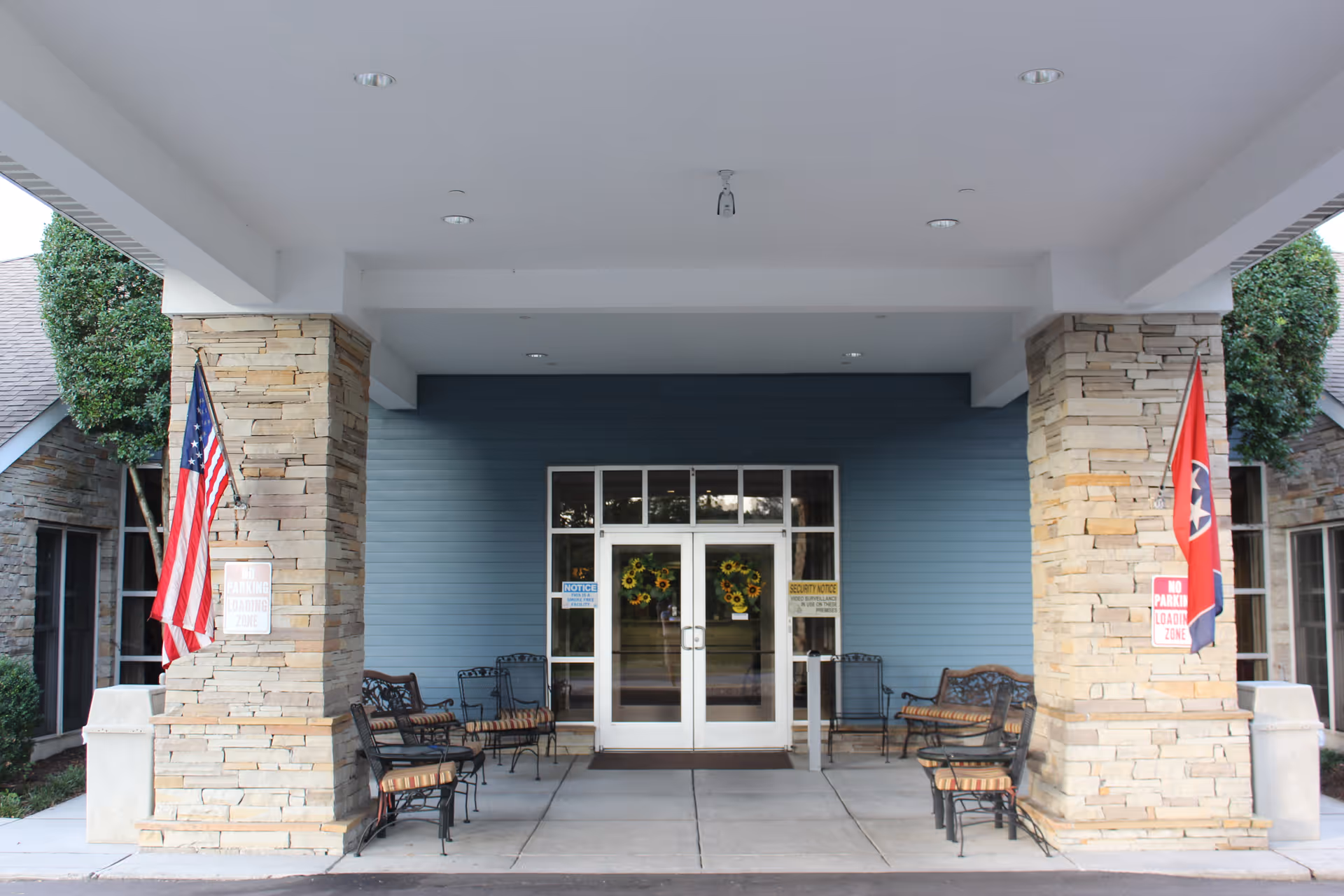 Covered main entrance to Windsor Ridge with stone pillars, glass double doors, benches, and American and Tennessee flags.