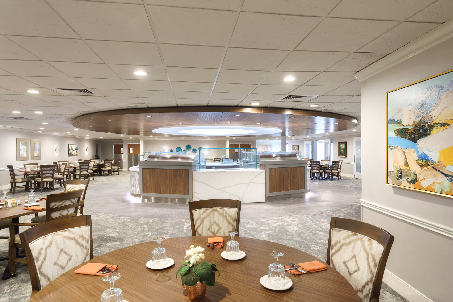 Spacious dining room with round tables set for service and a central buffet/service island beneath a circular ceiling feature.