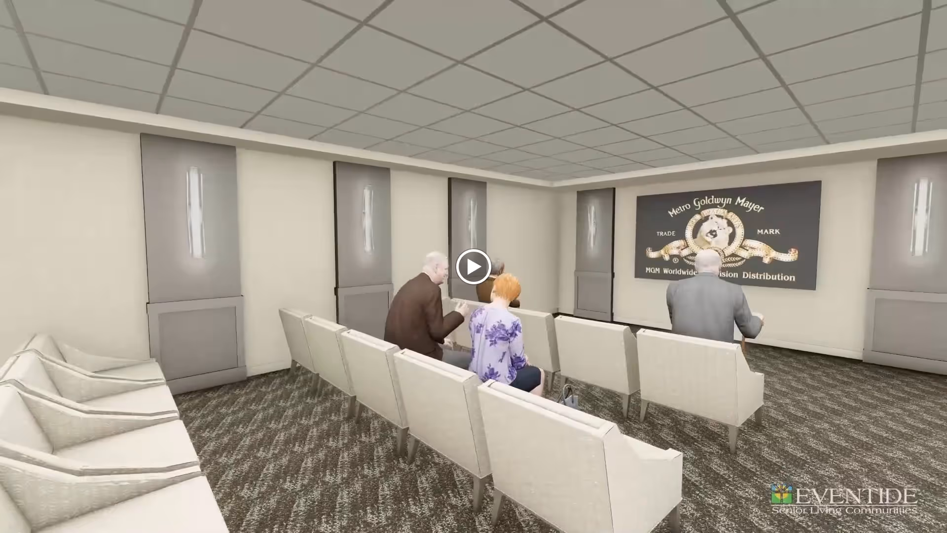 A small theater room with rows of beige chairs facing a screen displaying the Metro Goldwyn Mayer logo. Three elderly people are seated, watching the screen. The room has beige walls, carpeted floor, and modern wall sconces.
