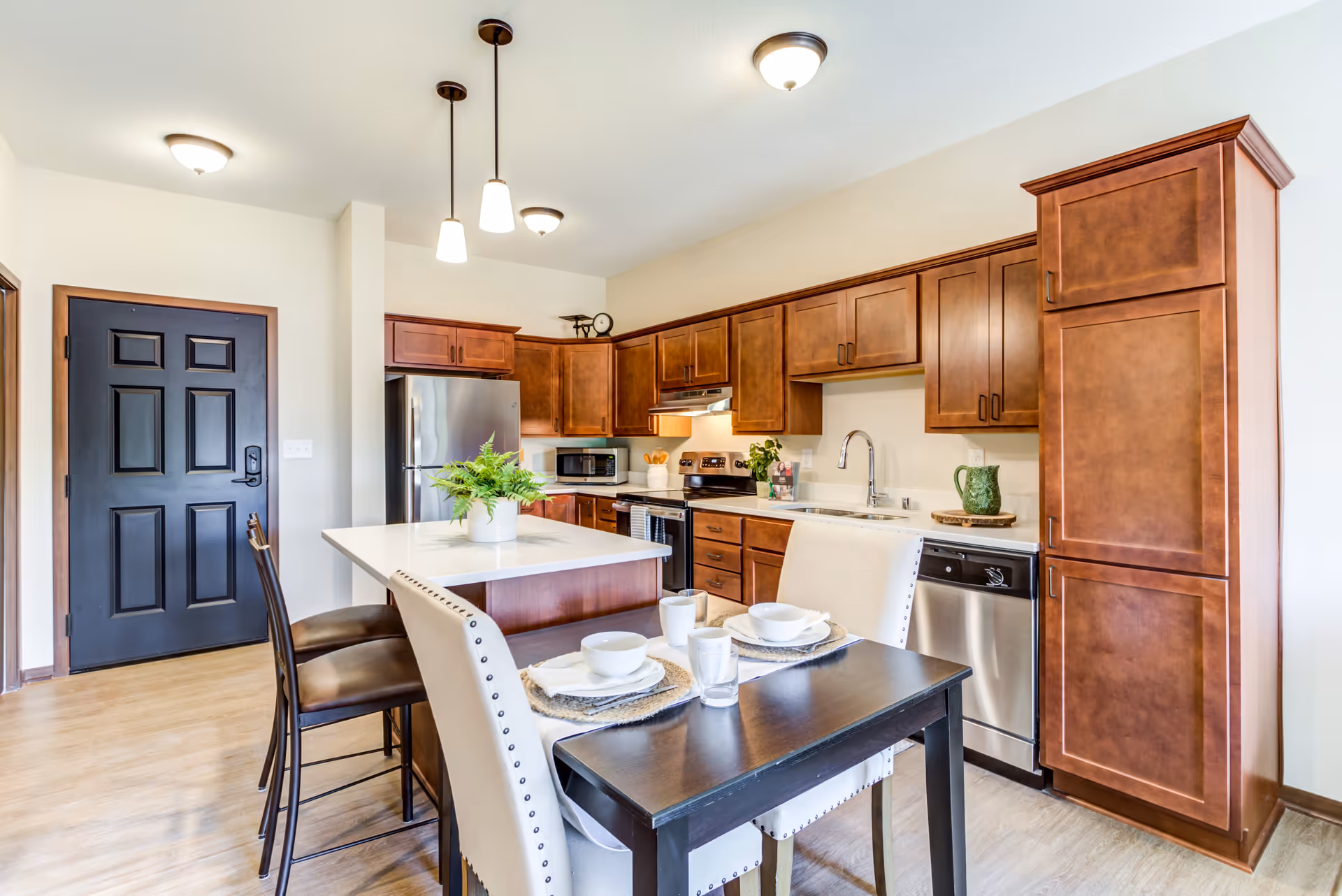 Bright modern kitchen with wooden cabinets, stainless steel appliances, an island and a small dining table set for two.