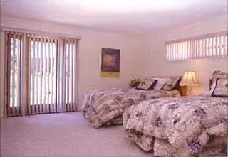 Two twin beds with floral quilts, nightstand lamps, and sliding glass doors in a bright bedroom.
