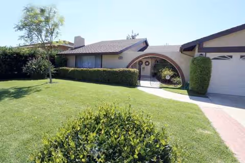 Front exterior of Whispering Oaks Senior Living facility with green lawn and arch entry.