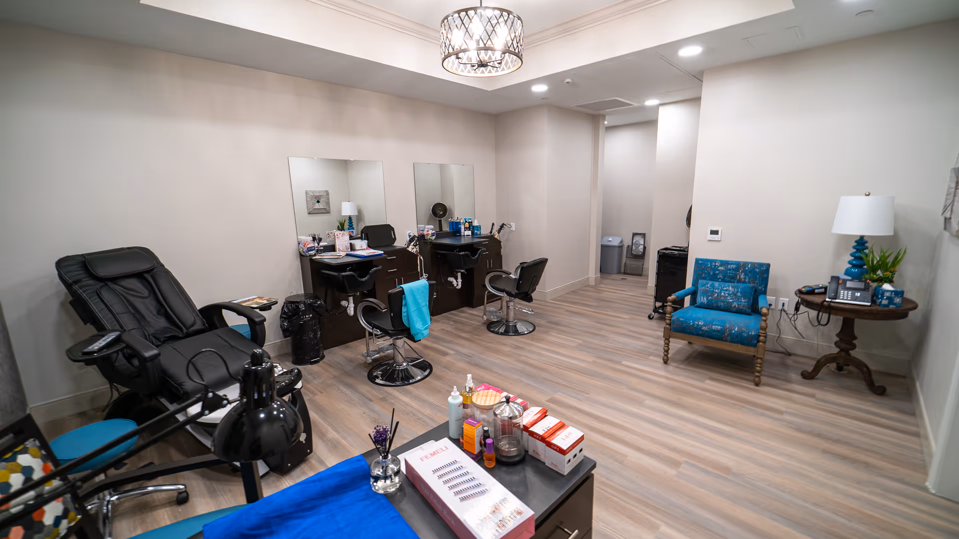 A bright interior salon room with manicure and pedicure stations, reclining chairs, and a small seating area.