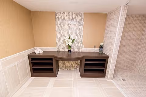 Tiled spa-like room featuring a dark wooden vanity with open shelves, a vertical mosaic accent strip on the wall, and a tiled shower area to the right.