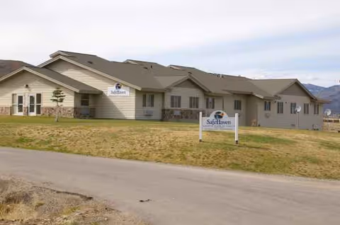 Single-story care facility exterior with signs, grassy lot, and distant mountains.