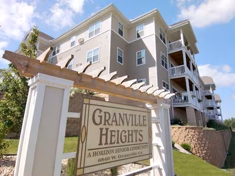 Exterior view of a multi-story senior apartment building with balconies under a blue sky, featuring a wooden pergola structure holding a sign that reads 'Granville Heights, A Horizon Senior Community, 6840 W. Granville Ct.'