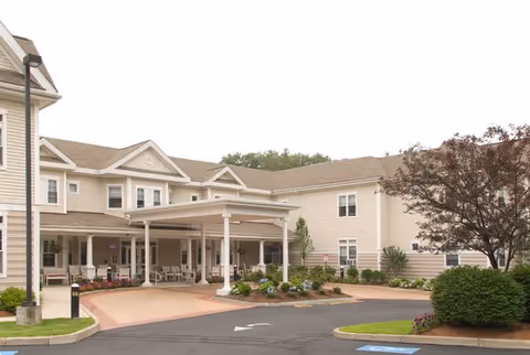 Exterior view of a beige senior living facility with a covered entrance and parking.