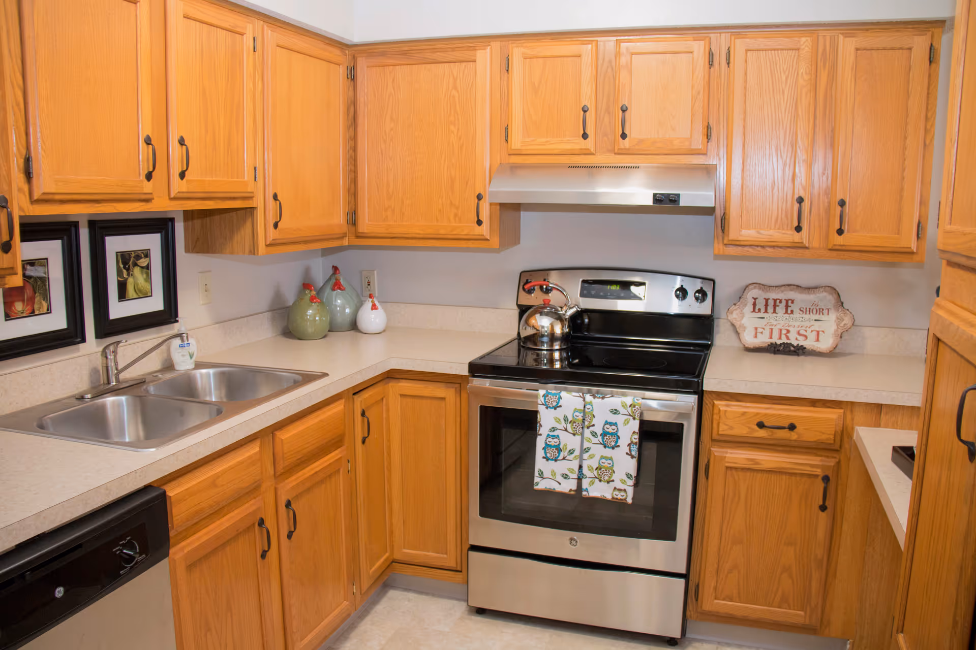 Compact kitchen with oak cabinets, double sink, stainless steel stove and small decorative items on the countertops.