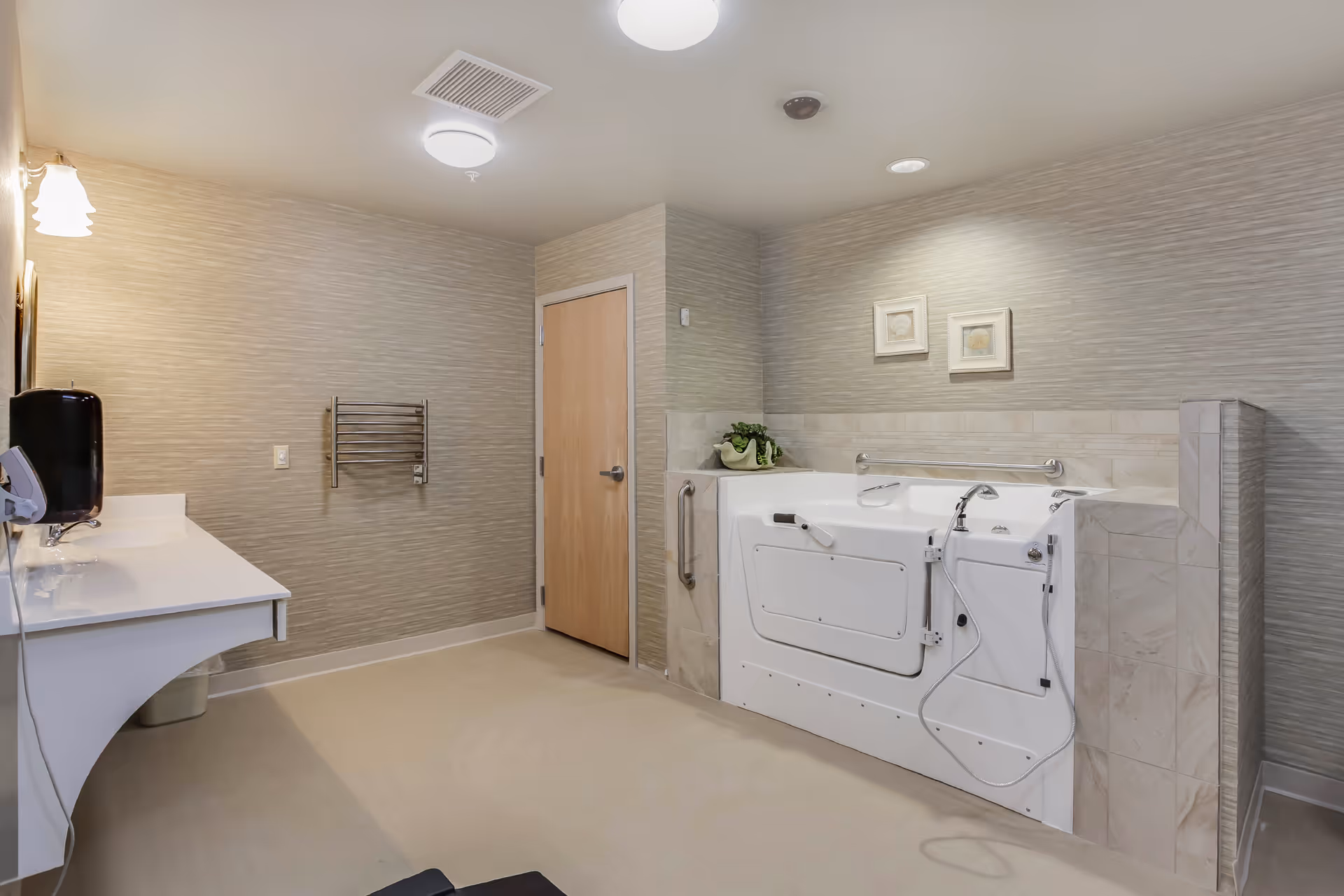 Accessible bathroom featuring a walk-in bathtub with grab bars, a sink countertop, towel rack, and a closed wooden door.