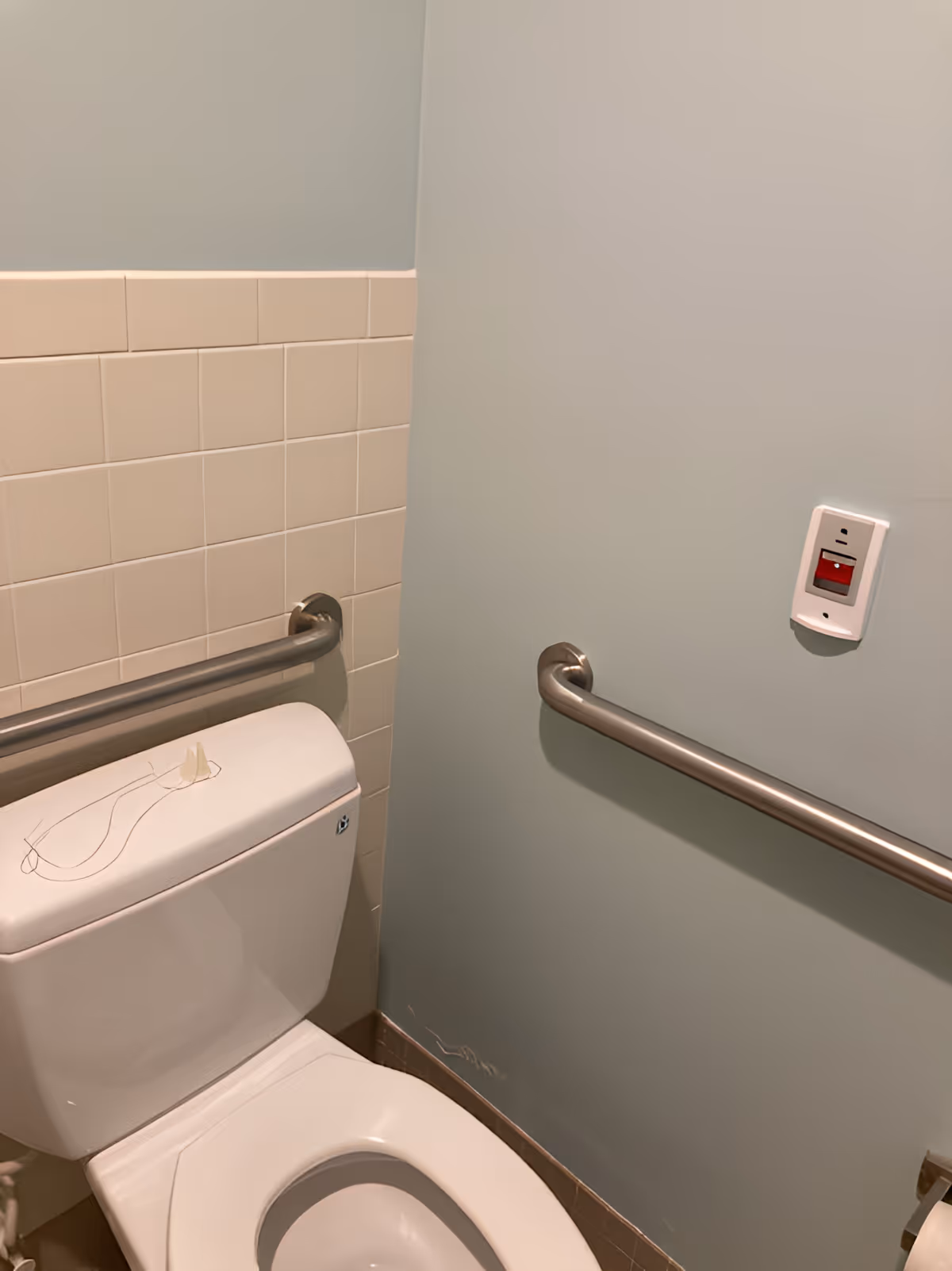 Accessible bathroom with a toilet, wall-mounted grab bars, tiled wall, and an emergency call button.