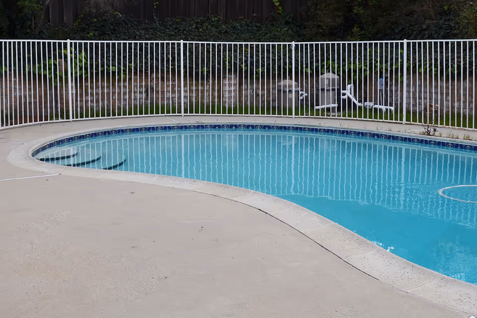 Outdoor fenced swimming pool with a concrete deck and clear blue water.