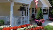 Front porch of Arden Courts Avon with white railing, planters, and an American flag.