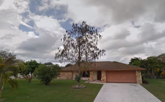 Single-story brick house with a two-car garage, front yard, and cloudy sky.