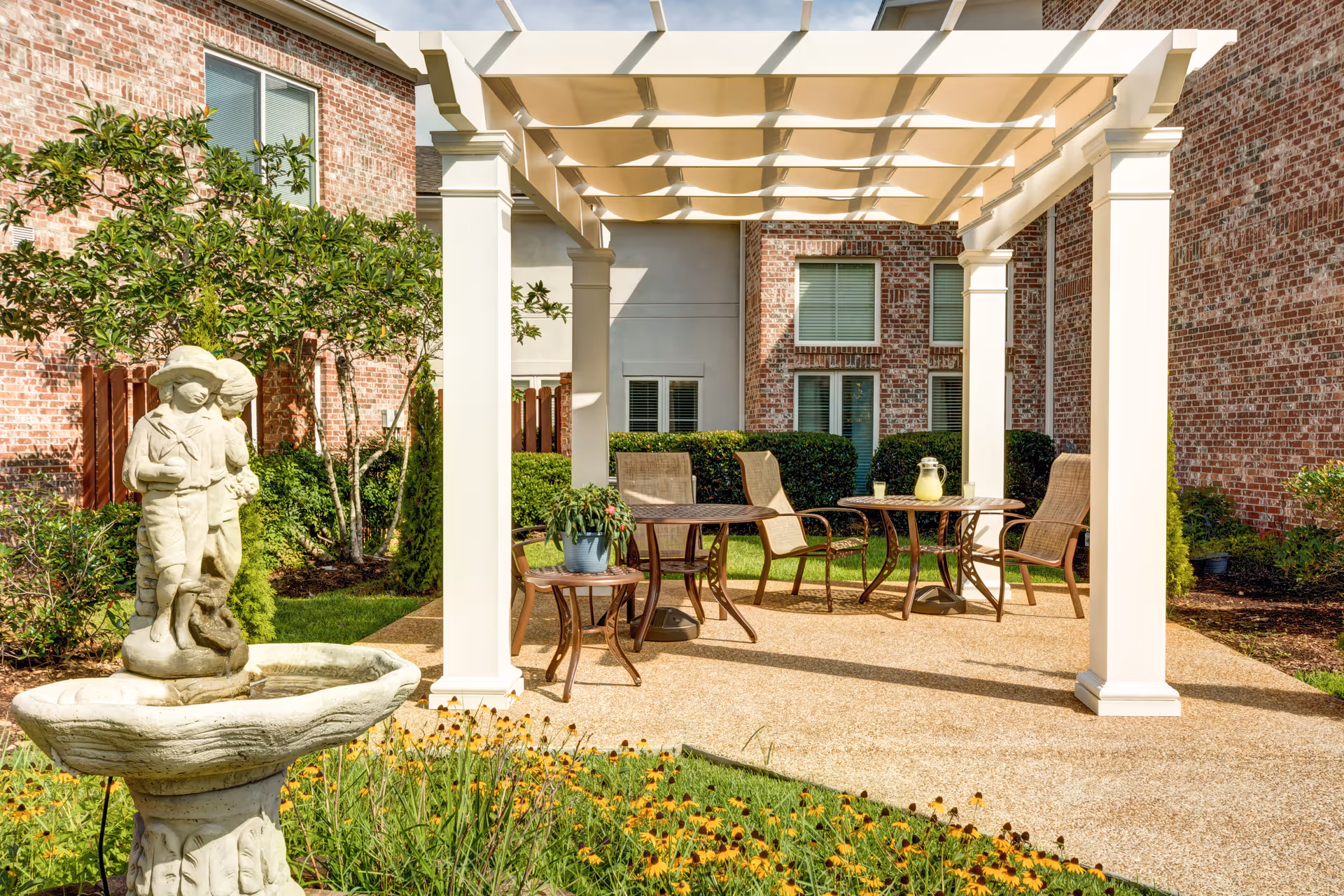 Outdoor courtyard with a pergola, patio table and chairs, a statue fountain, and a brick building backdrop.