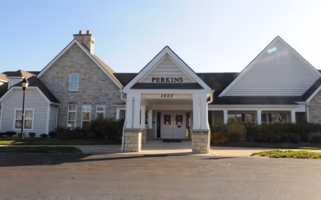 Front entrance of a one-story building with a covered portico marked 'PERKINS'.