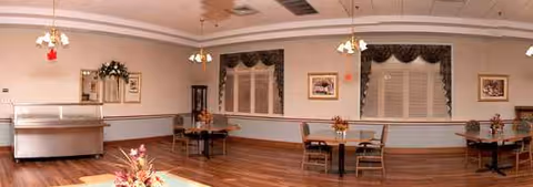 Spacious dining room with tables, chairs, and a serving counter in a nursing home.